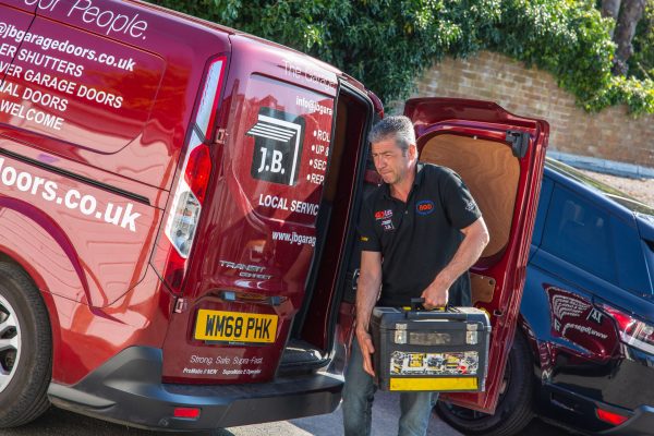 JB Garage Doors employee carrying tool box out of back of red company van